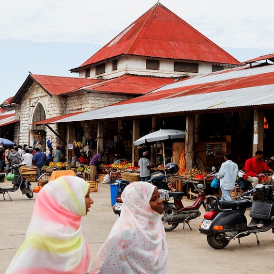 A bustling market with vendors and shoppers, a prominent red-roofed building, and motorcycles. 2