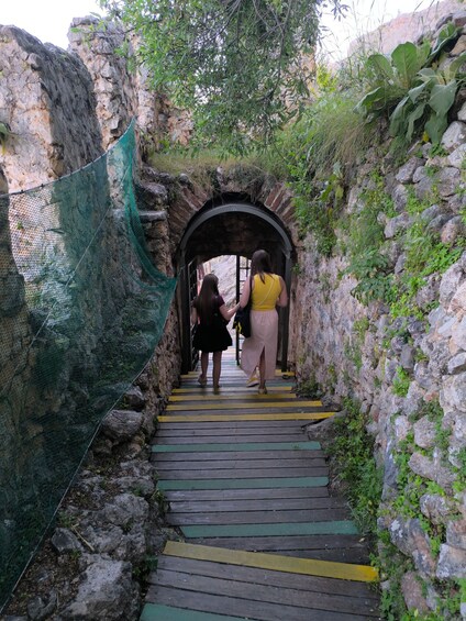A narrow stone pathway with a green net on one side, leading to an arched stone entrance. 2