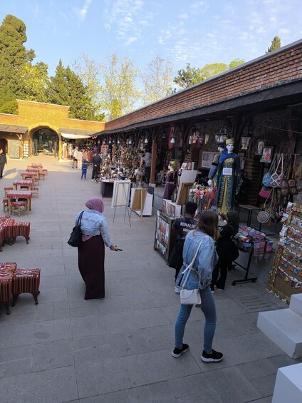 A bustling outdoor market with various stalls selling textiles, bags, and accessories. 4
