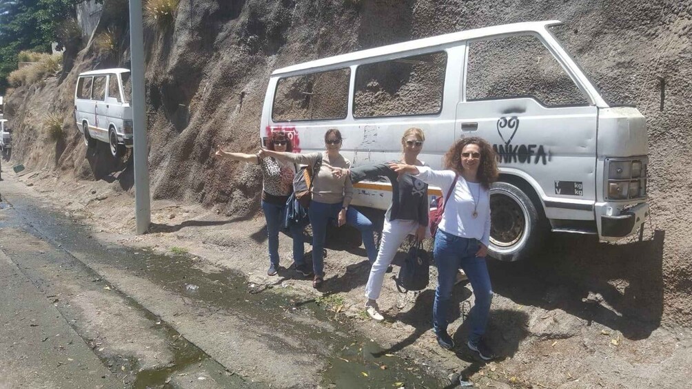 A white van parked by a rocky roadside with a group of people standing beside it. 2