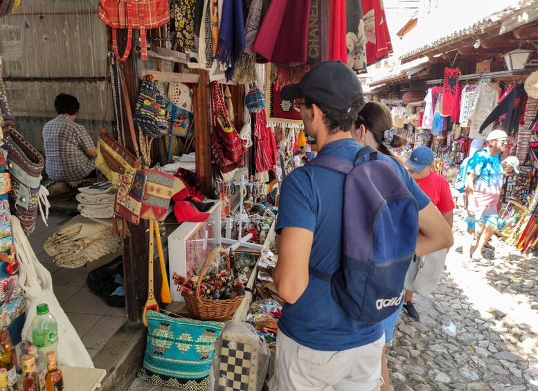 A bustling outdoor market with various stalls selling textiles, bags, and other goods. 3