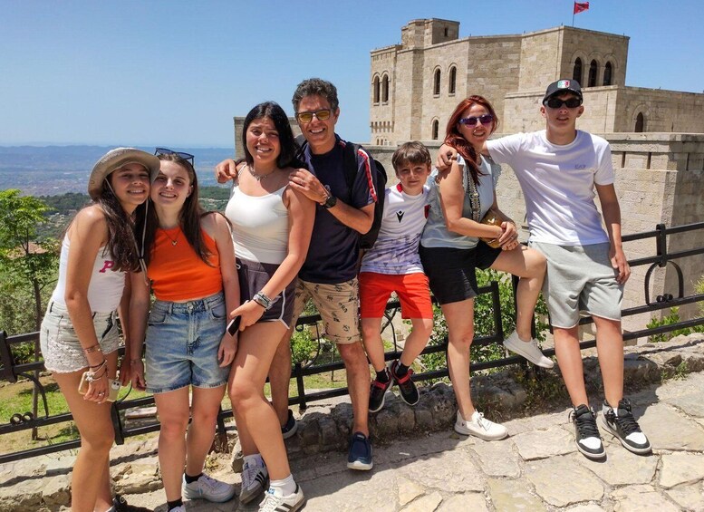 A group of people posing in front of a historic stone building with a flag on top, overlooking a scenic landscape. 4