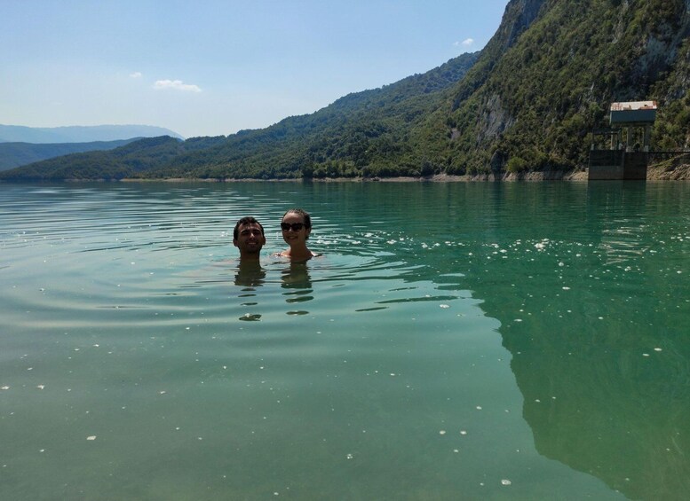 Two people swimming in a calm lake with mountains in the background. 2