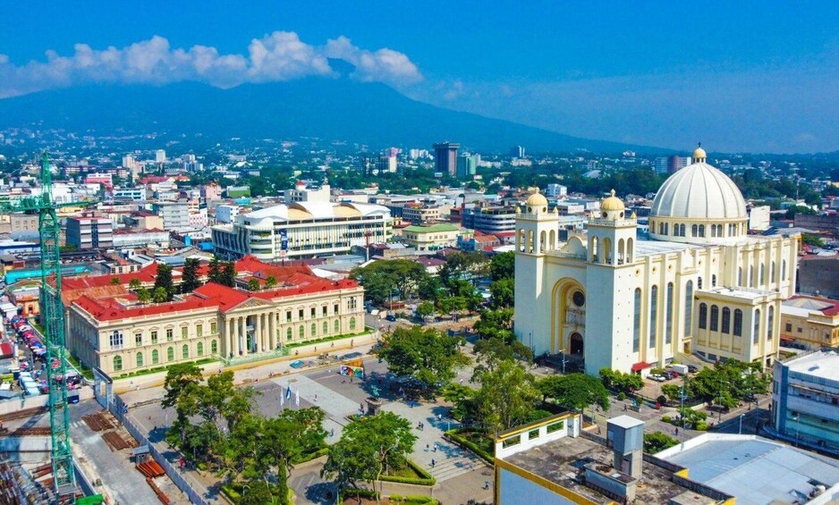 A cityscape with a prominent cathedral, a large green building, and a mountain in the background. 3