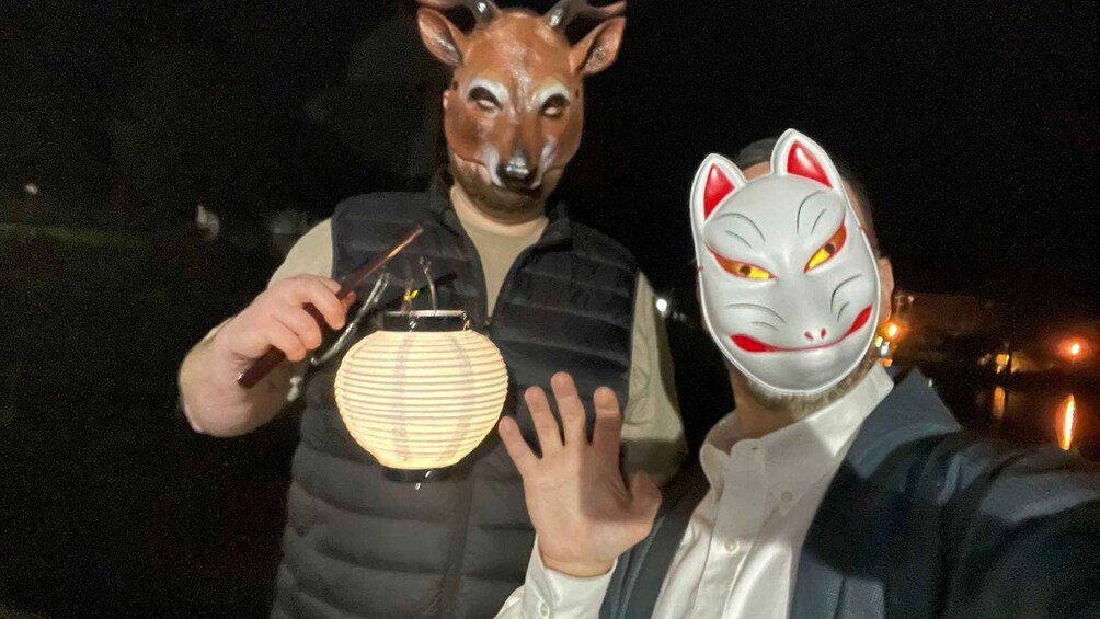 Two people wearing animal masks, one with a deer head and the other with a cat face, holding a lantern. 2
