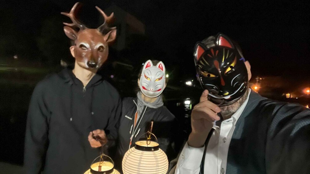 Two people wearing masks, one with deer antlers and the other with a cat mask, holding a lantern. 5