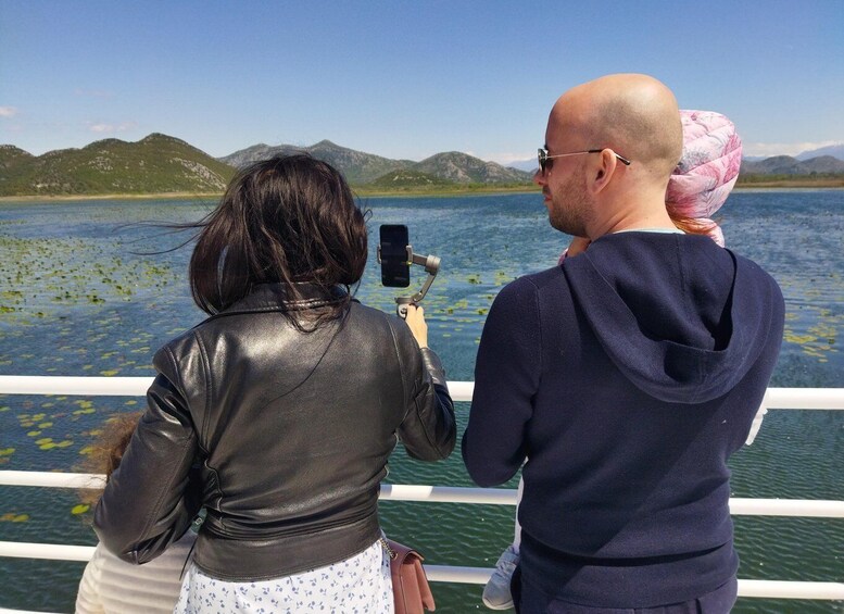 Two people taking a photo of a lake with mountains in the background. 3