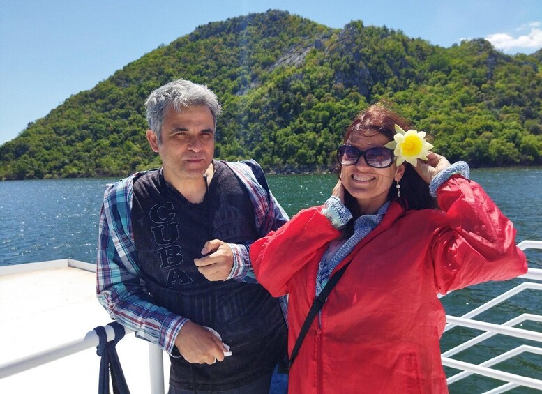 Two people on a boat with a mountainous landscape in the background. 2