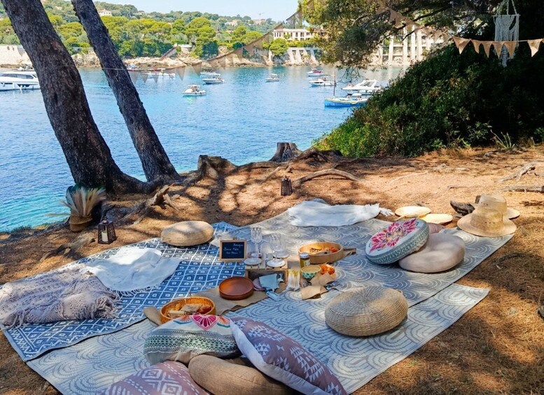 A picnic setup with a blanket, food, and drinks on a beach with boats in the background. 2