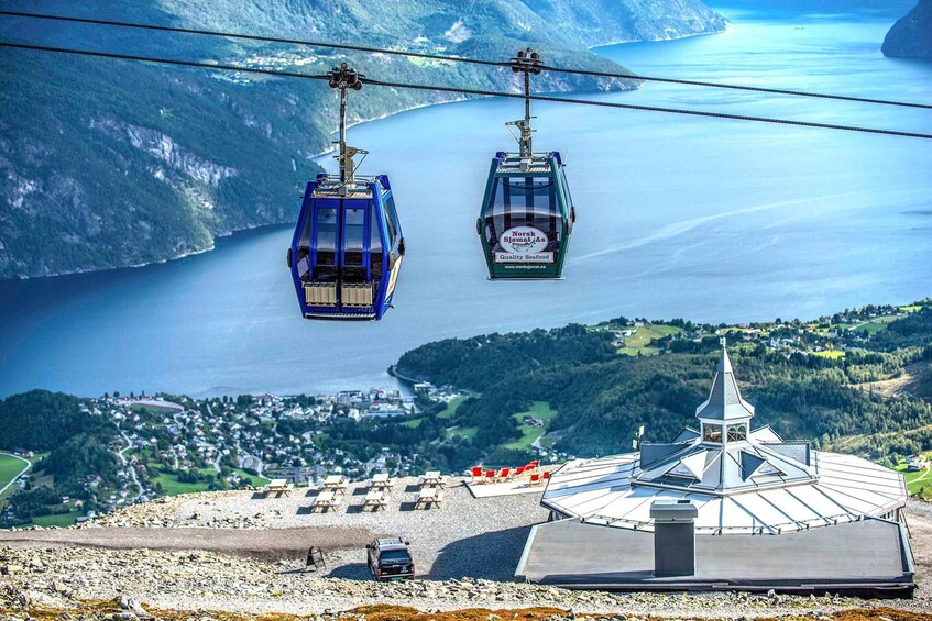 Two cable cars over a fjord, a church, and a village below. 2
