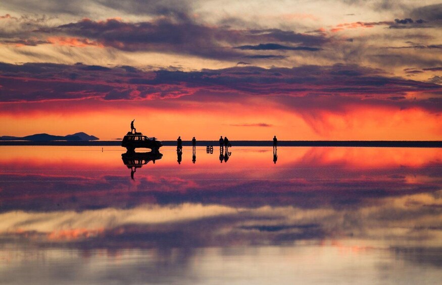A sunset over a calm lake with a boat and people silhouetted against the sky. 5