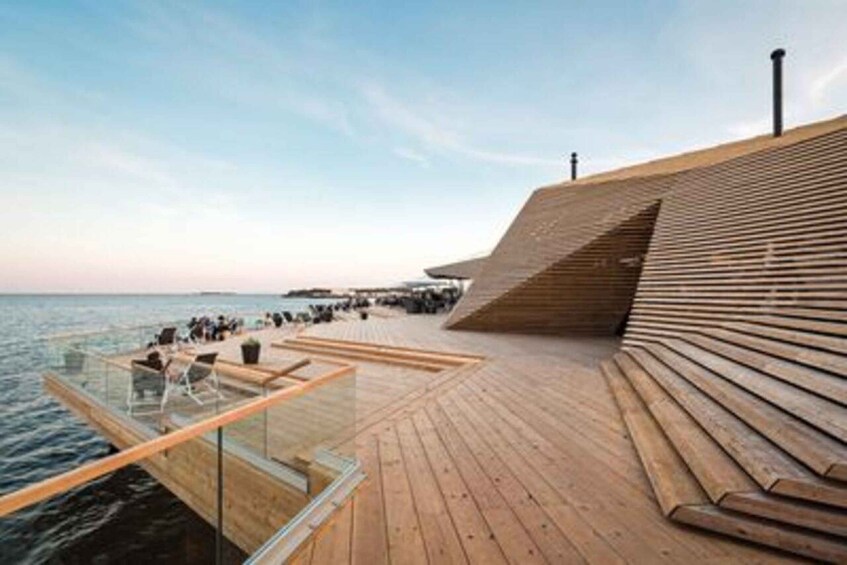 A wooden deck extending over water with seating and a glass railing. 3