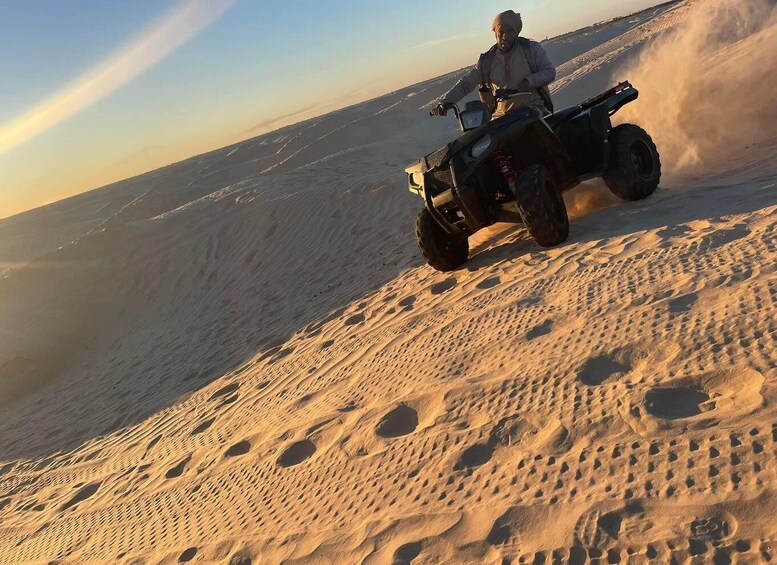 A person riding an ATV on a sandy terrain with footprints and a clear sky. 1