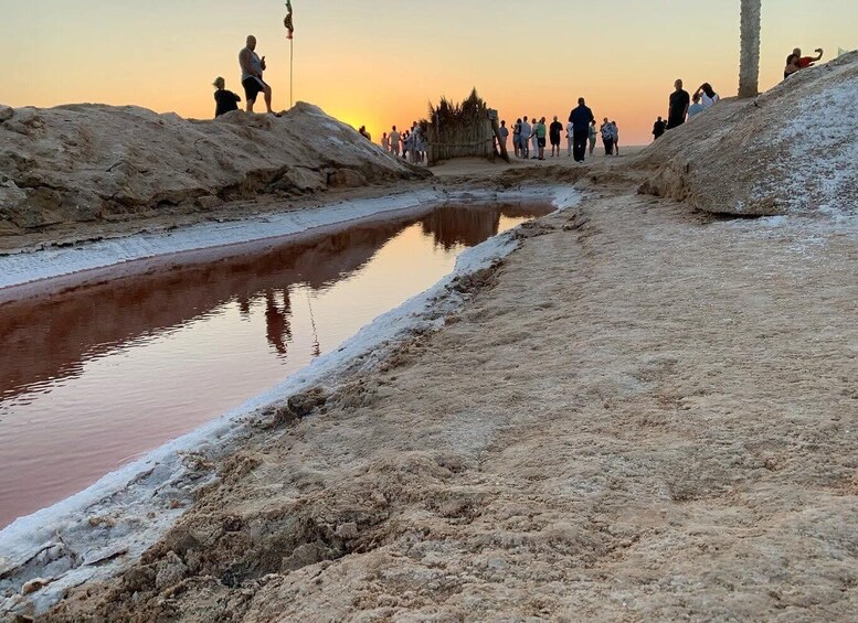 A group of people walking along a sandy path beside a calm water channel during sunset. 5