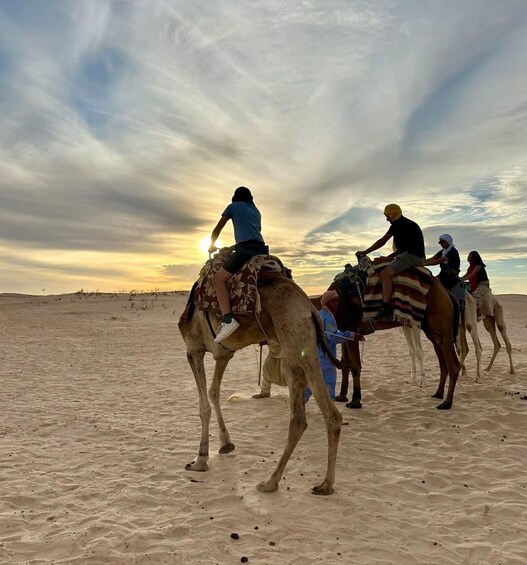 A group of people riding camels in a desert landscape during sunset. 4