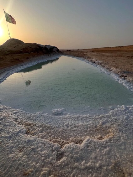 A salt flat with a flag on a dune, clear sky, and a calm water body. 2