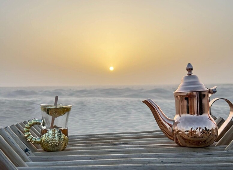 A teapot and a glass on a wooden surface with a sunset over the ocean. 3