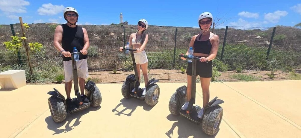 Three people on segways in an outdoor area with a fence and trees in the background. 1