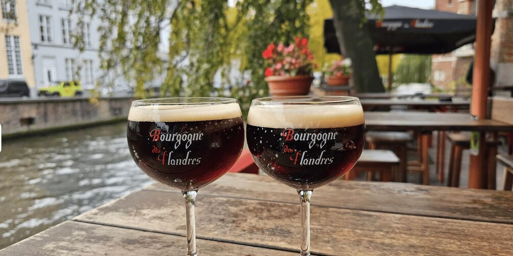 Two glasses of burgogne des fandes on a wooden table with a river and buildings in the background. 4