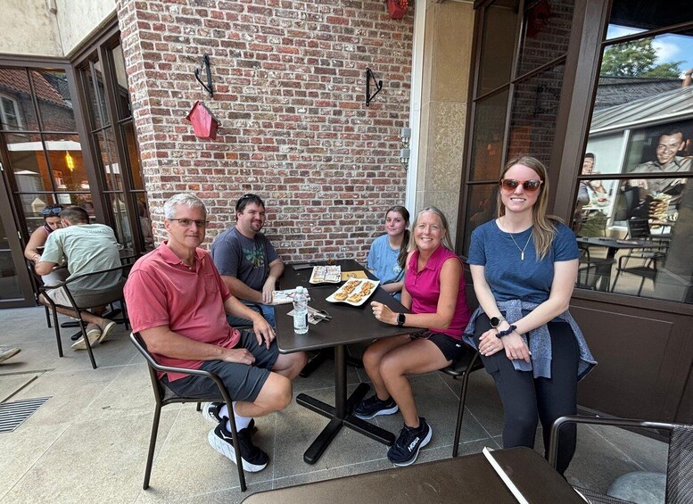 A group of people sitting at an outdoor table with food, in front of a brick building with large windows. 3