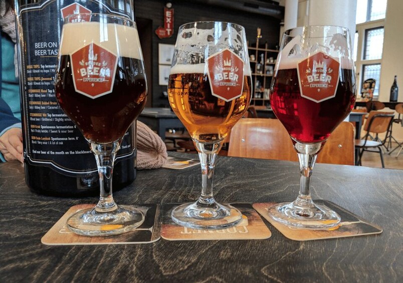 Three glasses of beer on a table with coaster mats, each with a logo. 5