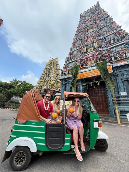 A green auto-rickshaw with passengers in front of a temple with intricate carvings. 1