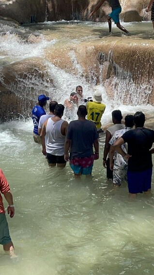 A group of people wading through a shallow water channel with a rocky waterfall. 4