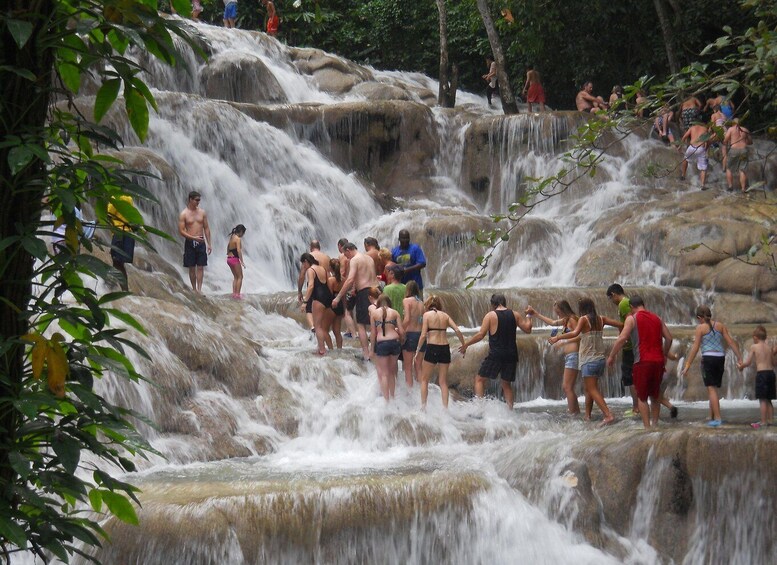 A waterfall with people standing on rocks and swimming in the water. 1