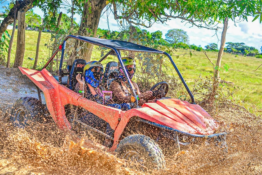 A red off-road vehicle driving through a muddy field with water splashing around. 1