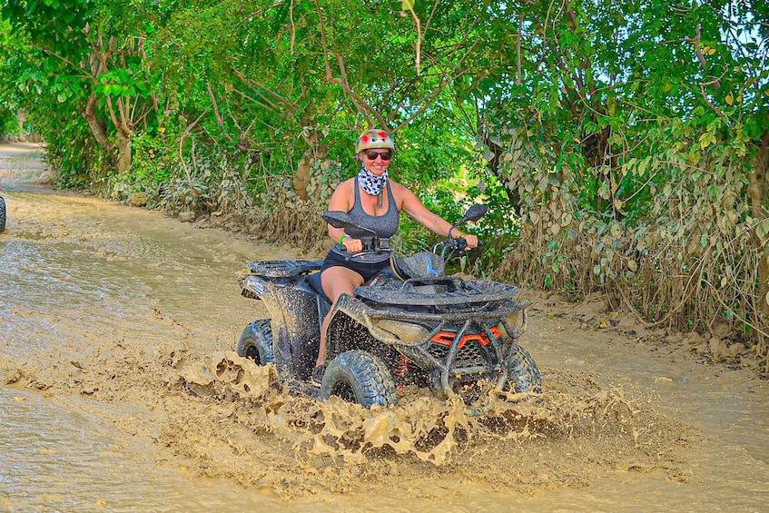 A person riding a quad bike through a muddy path surrounded by dense greenery. 4
