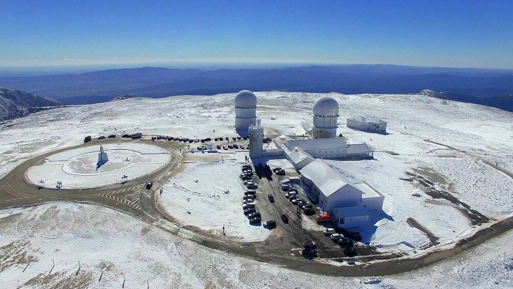 A snow-covered facility with two domed structures, a circular driveway, and parked vehicles. 5