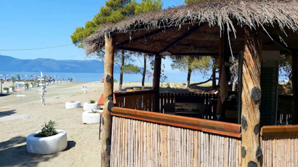 A beachside wooden structure with a thatched roof, surrounded by sand and potted plants. 4