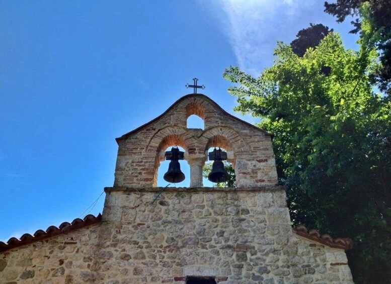 A stone bell tower with two bells and a cross on top. 1