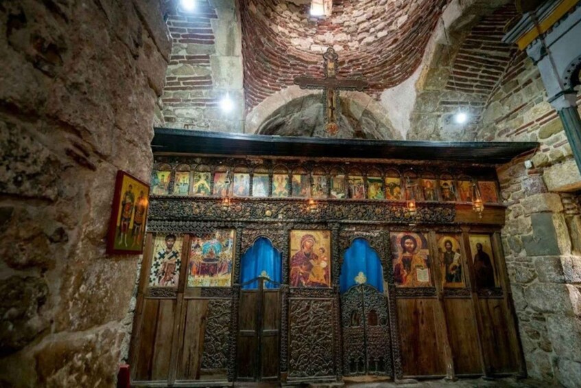 An interior of a church with wooden iconostasis, stone walls, and a cross on the ceiling. 5