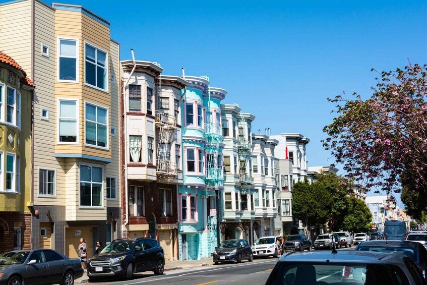 A street lined with colorful Victorian-style buildings, parked cars, and a clear blue sky. 5