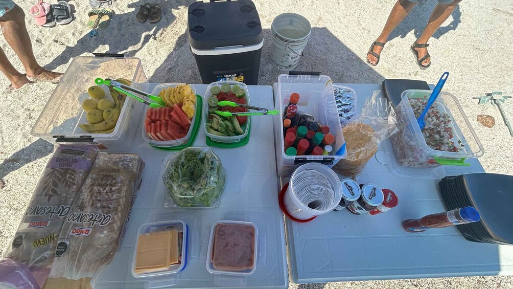 A table with various food items and containers, including fruits, vegetables, and condiments, set outdoors. 3