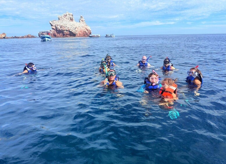 A group of people snorkeling in the ocean with a rocky formation in the background. 1