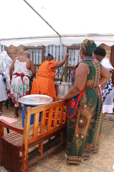 People in traditional attire at an outdoor event, with a tent and a table with a metal container. 4
