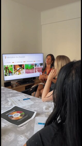 A group of people sitting at a table with a laptop displaying a presentation about chocolate production. 3