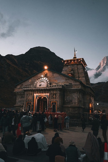 A stone building with a clock and a dome, surrounded by mountains and a crowd of people. 1