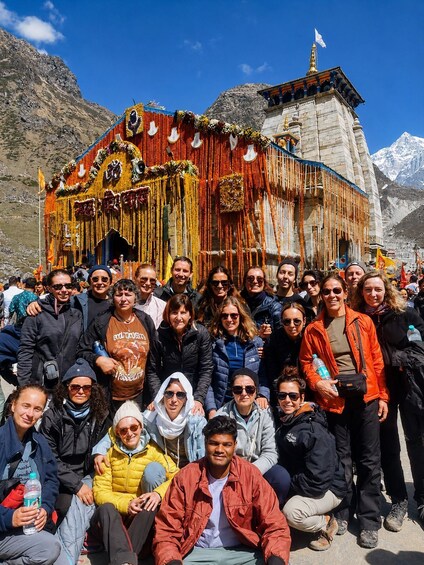 A group of people in front of a colorful, ornately decorated building with a flag on top, set against a mountainous backdrop. 2