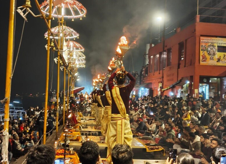 A nighttime street procession with people carrying flaming torches, a crowd watching, and a building with a poster in the background. 1