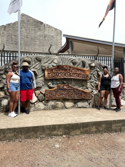 A group of people standing in front of a sign for The Museum of Natural & Cultural Heritage at Shai Hills. 3