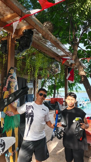 Two individuals near a wooden structure with a beach view, a decorative painting, and a hanging disco ball. 5