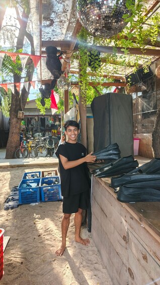 A person standing near a wooden structure with a tarp, surrounded by trees and a market in the background. 2