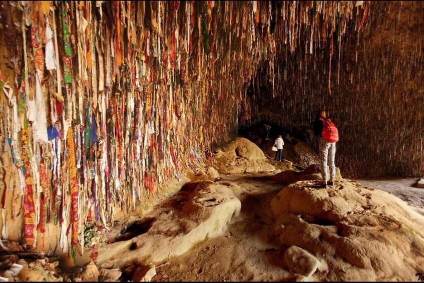 A cave with colorful prayer flags hanging from the ceiling and a person standing on a rock formation. 5