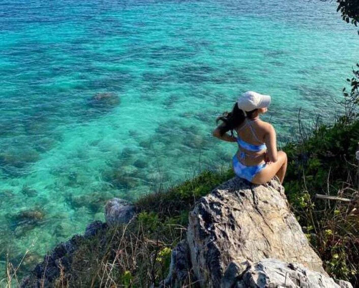 A person sitting on a rock by a clear blue sea. 3