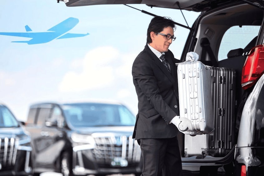 A man in a suit loading a suitcase into a car trunk. 3