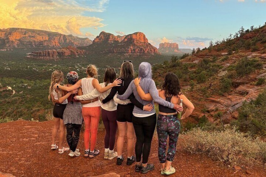 A group of people standing on a hill overlooking a canyon with red rock formations and a view of the valley below. 1
