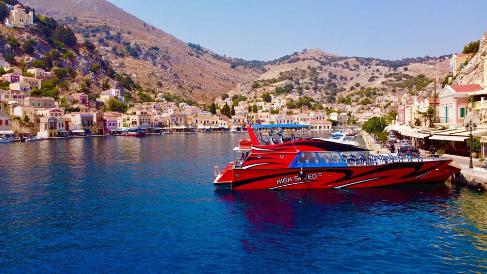 A red speedboat named 'HIGH SPEED' docked in a harbor with colorful buildings and hills in the background. 1